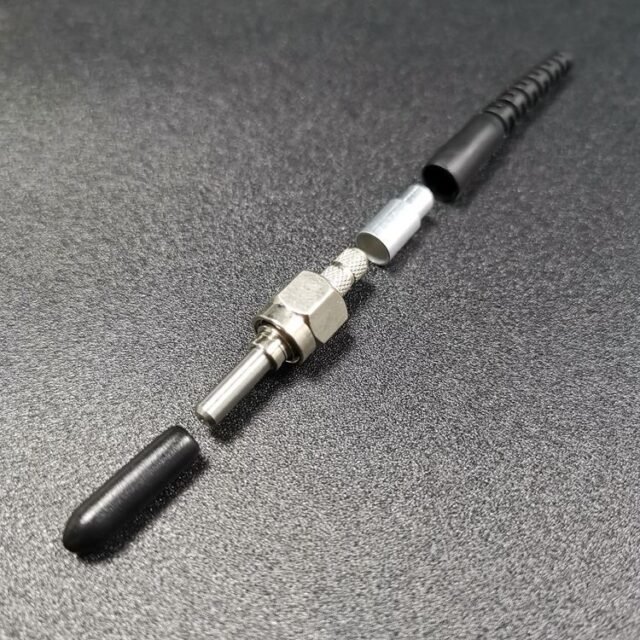 Exploded metal SMA905 connector assembly showing ferrule, knurled nut and black boot